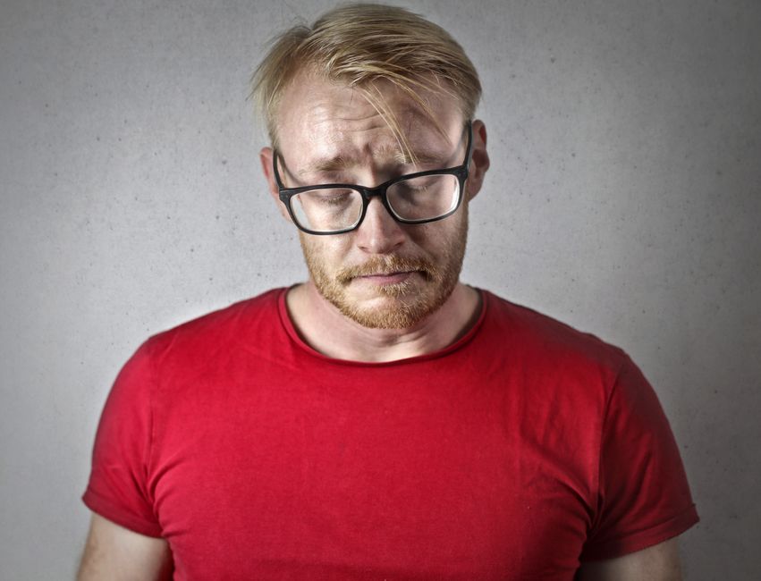 A man wearing glasses looks down with a mildly disappointed expression, illustrating the slang term "bummer."