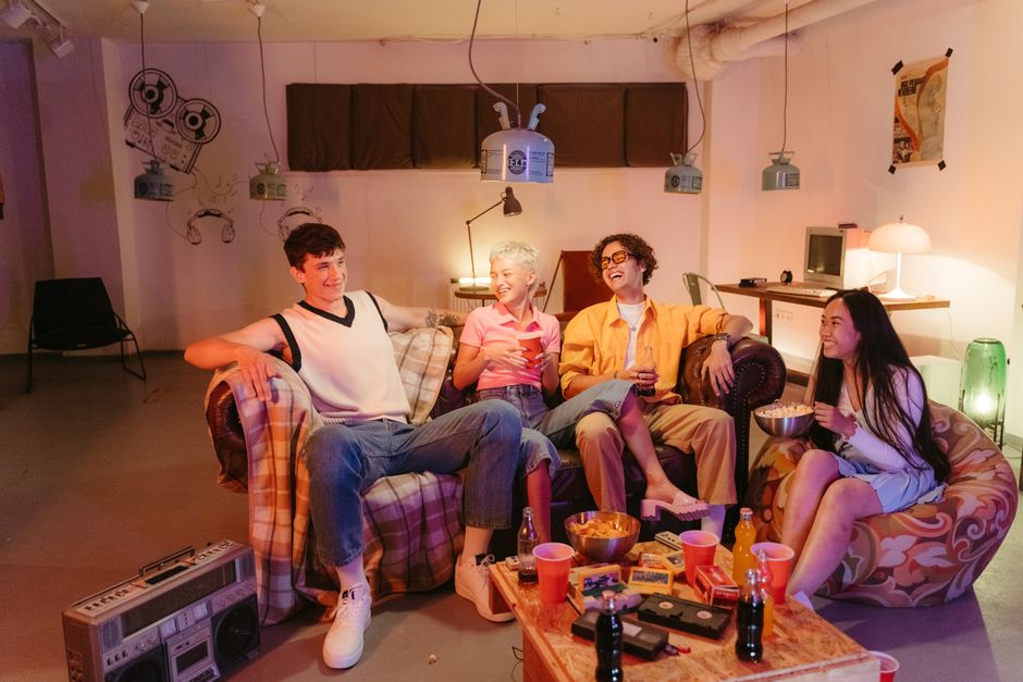 Friends relaxing together on cozy couches surrounded by snacks and a cluttered table, proving a messy house doesn't stop good company.