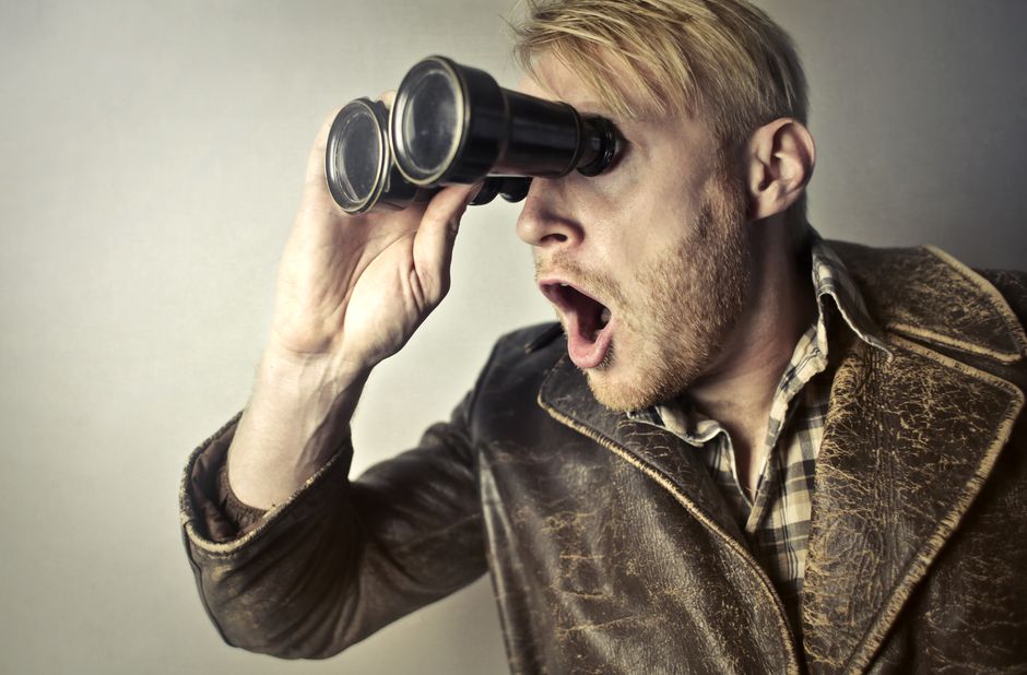 A man reacts with wide-eyed, mouth-open surprise while looking through binoculars, illustrating the vintage slang term "far out" for anything surprising.