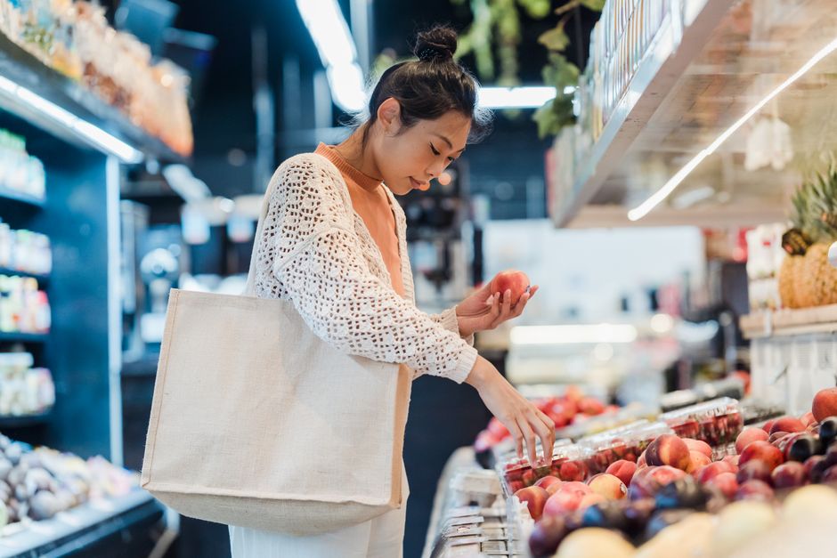A woman uses her folded reusable bag while picking out fresh produce at the grocery store.