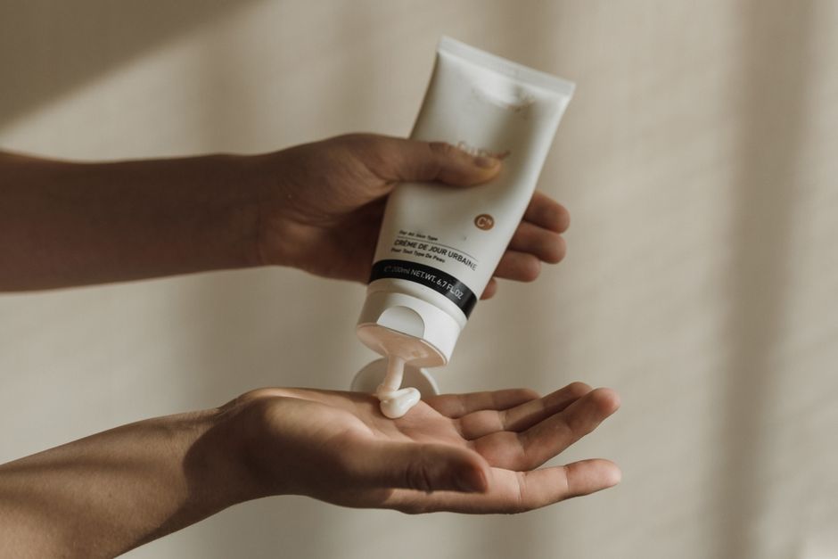 Hands squeezing a full size tube of lotion, too bulky to carry in a purse