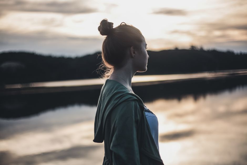 A woman pauses by the water at sunset, reflecting on life's wisdom and quietly contemplating change.