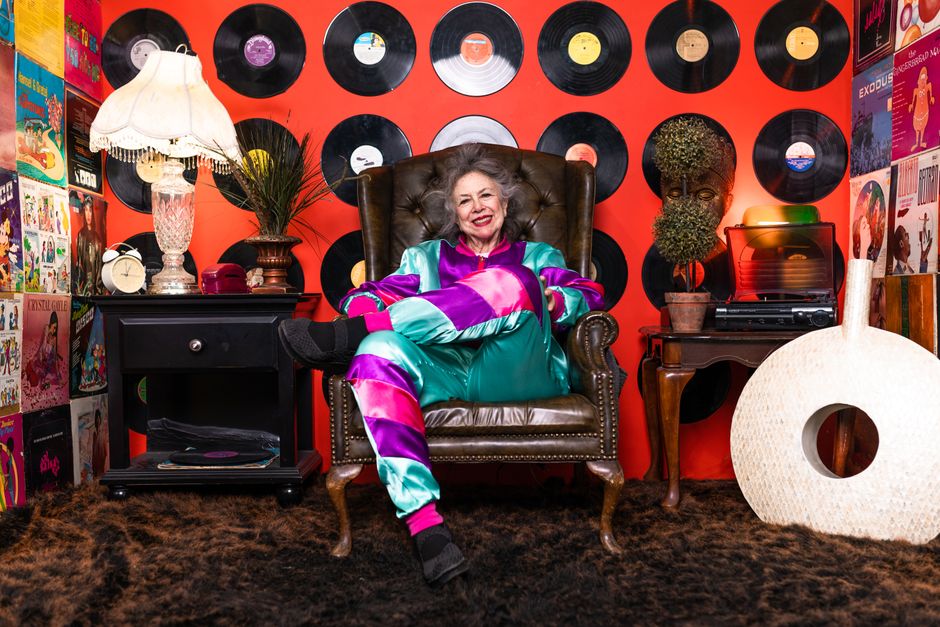A cheerful woman in a groovy tie-dye outfit lounges amid vintage records, capturing the retro vibe of old-school slang like 'groovy.'