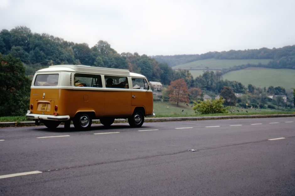 A vintage VW van keeps on truckin' down a scenic country road, a nod to classic slang only those born before 1980 would know.
