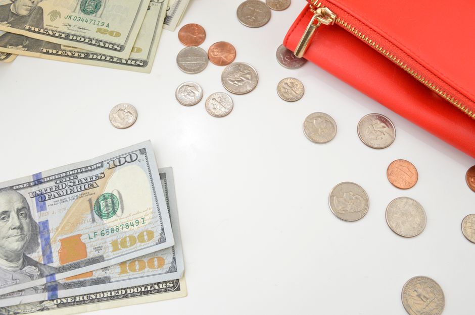 Loose change and bills spilling out near a red purse, ready to be sorted into a jar at home.