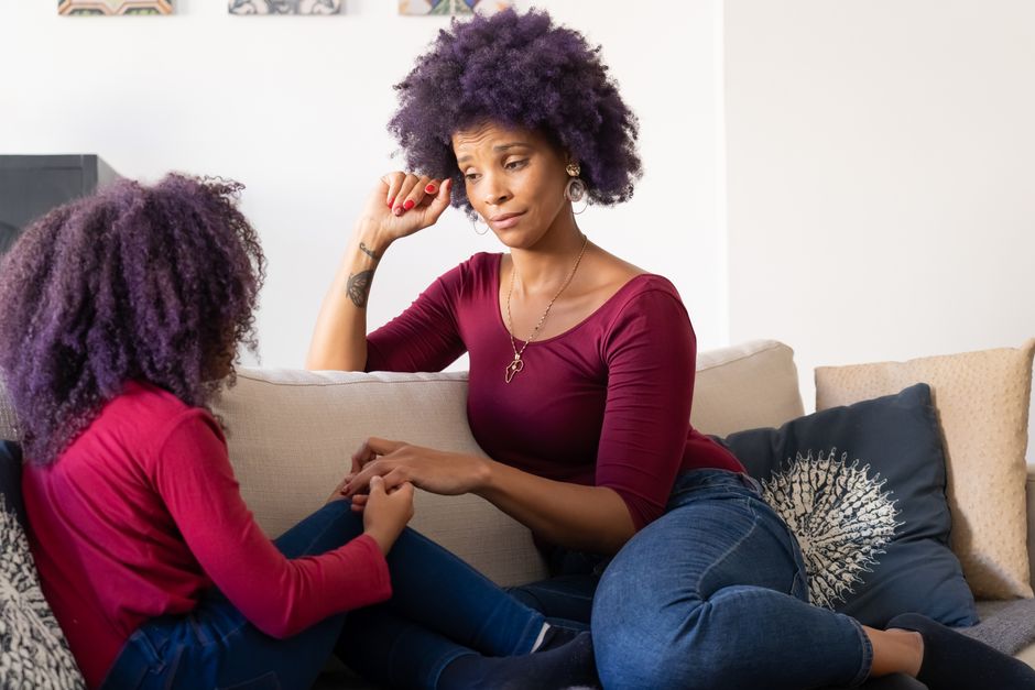 A mother and daughter hold hands during a heartfelt, serious conversation on the couch.