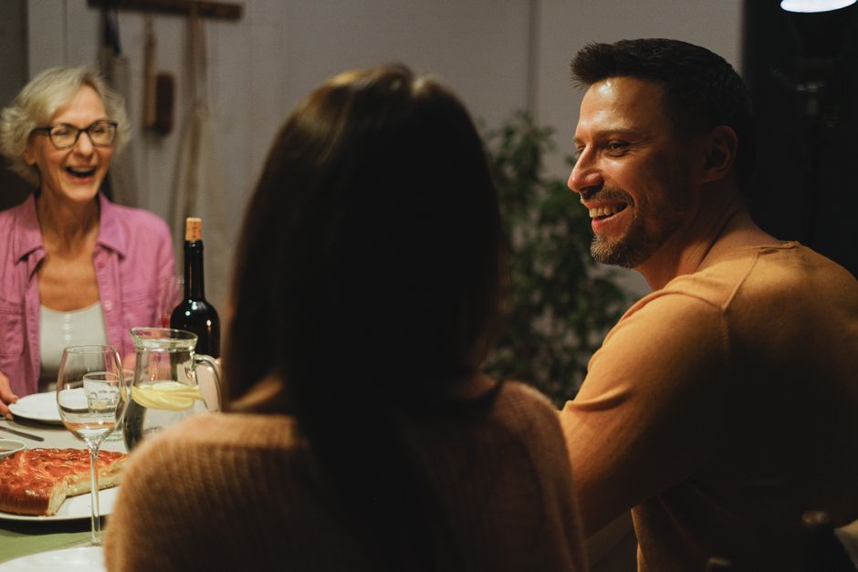 A mother laughing warmly with family at the dinner table, the kind of joyful moment worth asking her about when reflecting on the best day of her life.