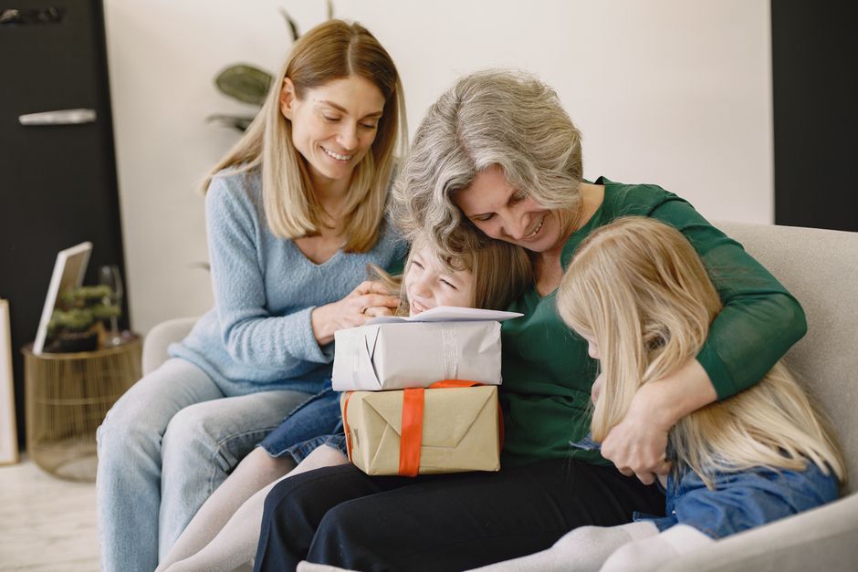 Grandmother, mother, and grandchildren share a tender, smiling moment together on the couch, reflecting on family memories.