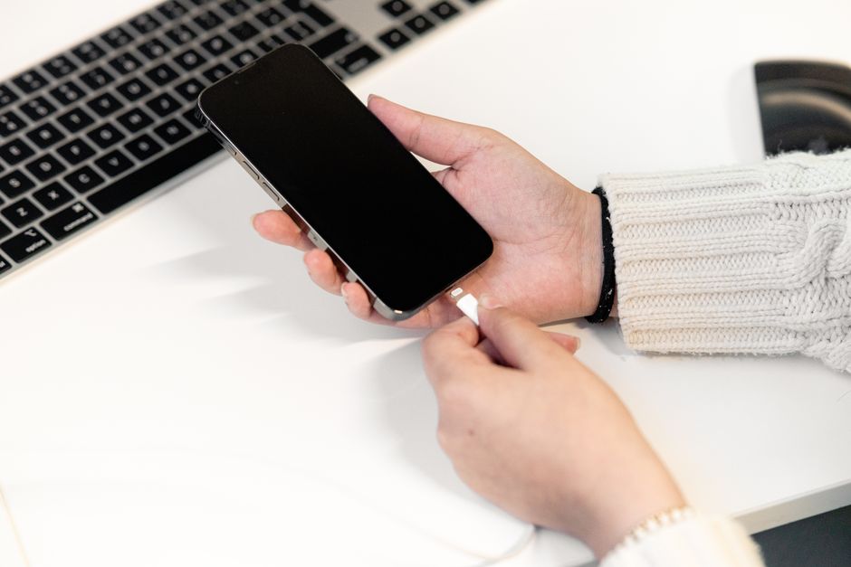 A woman plugs a charging cable into her phone, a reminder to clear out old cables that no longer fit your devices from your purse.
