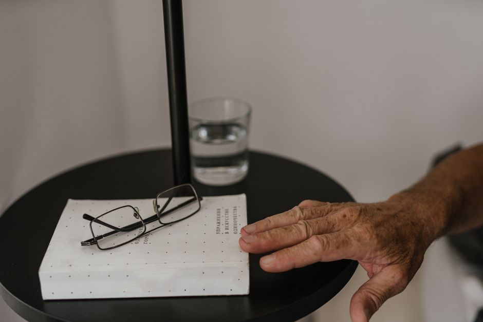 An elderly hand reaches for a glass of water on the nightstand, a simple habit that actually makes sense.