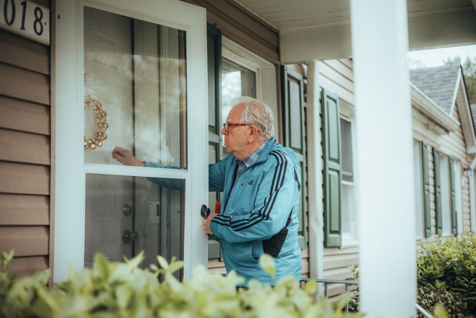 An older man checks his front door and keeps an eye on his neighborhood, reflecting the habit of staying alert to who's around for safety.
