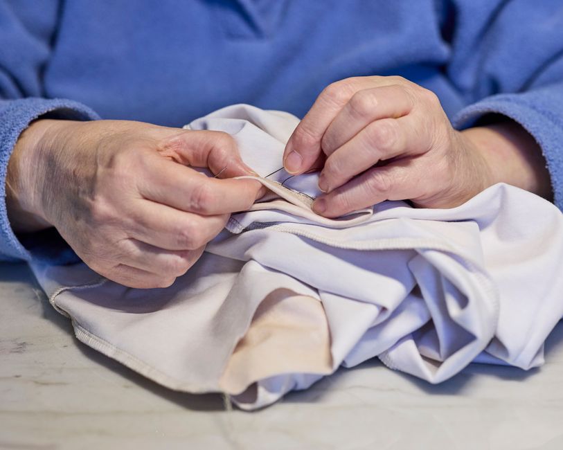 An older person's hands carefully mending a torn white garment by hand with needle and thread.