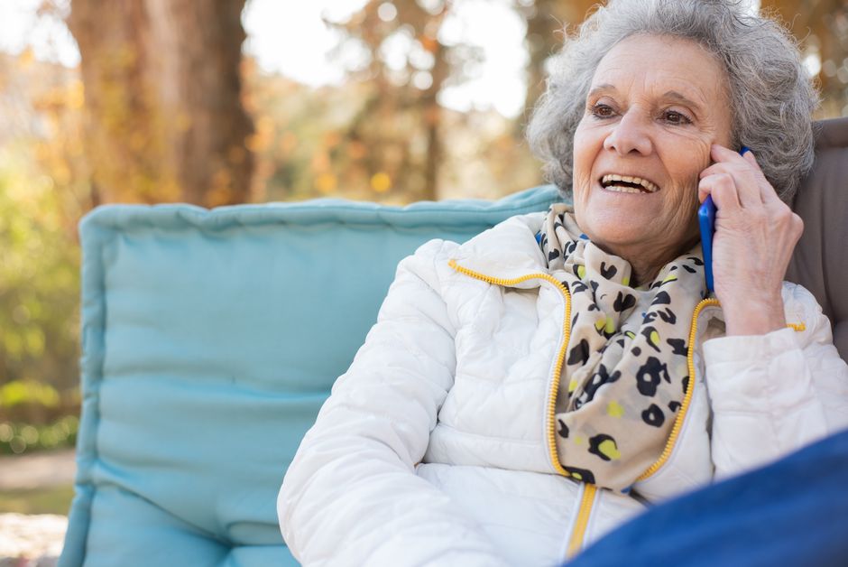 Senior woman happily calling someone on her phone outdoors instead of texting.