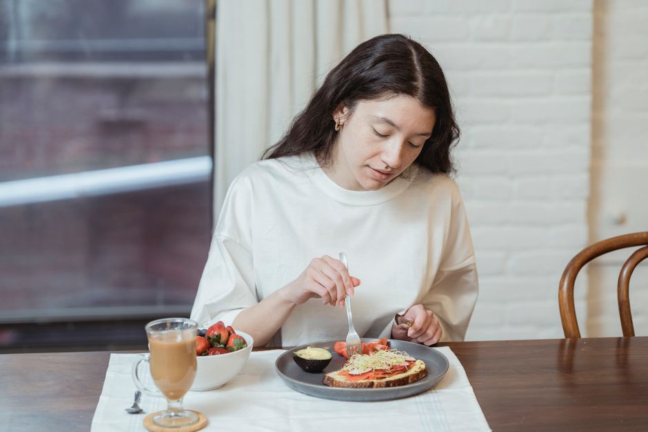 A woman enjoys her familiar daily breakfast of toast, fruit, and coffee at the table.