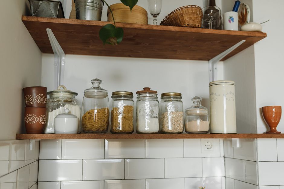 Reused glass jars and containers neatly storing pasta, rice, and flour on a kitchen shelf, reflecting old-fashioned thrift habits.