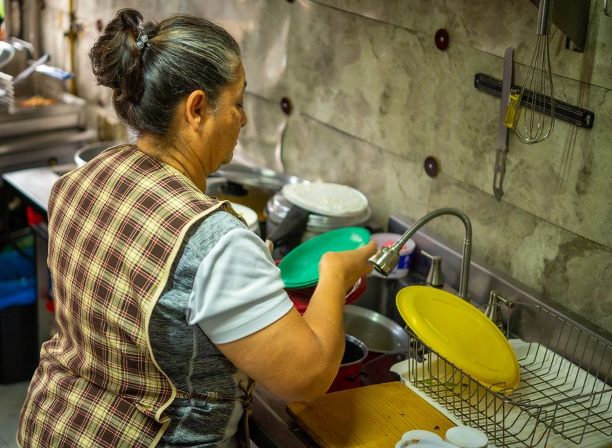 An older woman washing dishes at her kitchen sink right after a meal, embodying a timeless habit that still makes sense today.