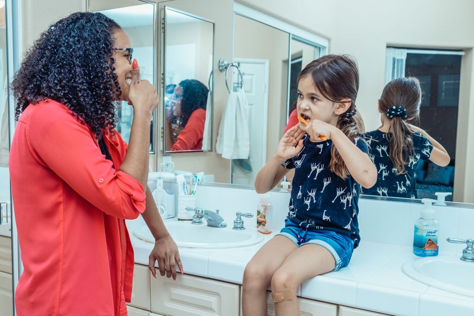 A mother and daughter mirror each other's routines at the bathroom sink, showing how kids learn by watching the way we care for ourselves.