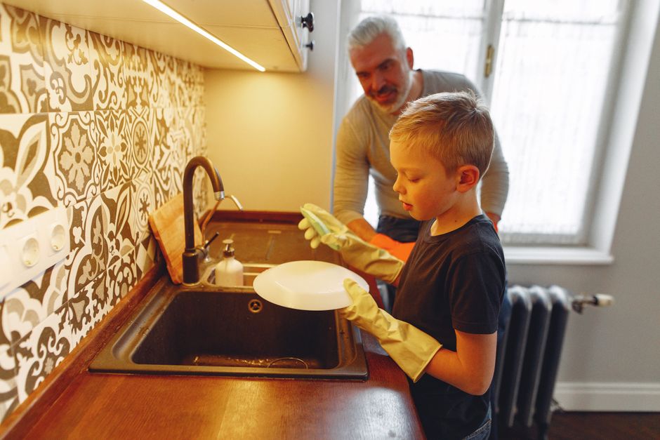 A parent patiently teaches his child how to wash dishes, taking the time to pass on the chore instead of just doing it himself.