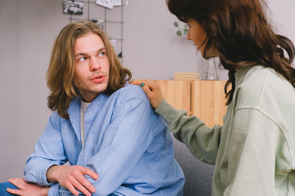 A woman listens attentively and offers comfort by placing her hand on a man's shoulder during a heartfelt conversation.