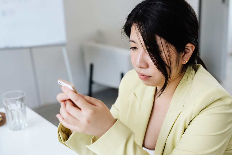 A woman pauses thoughtfully while looking at her phone, taking her time before responding.