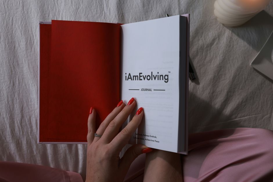 A person reflecting on their personal growth journey while journaling in an "iAmEvolving" notebook, symbolizing self-comparison and progress over time.
