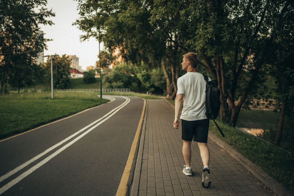A man takes a peaceful solo walk along a park path, embracing the simple wisdom that a short walk can clear the mind.