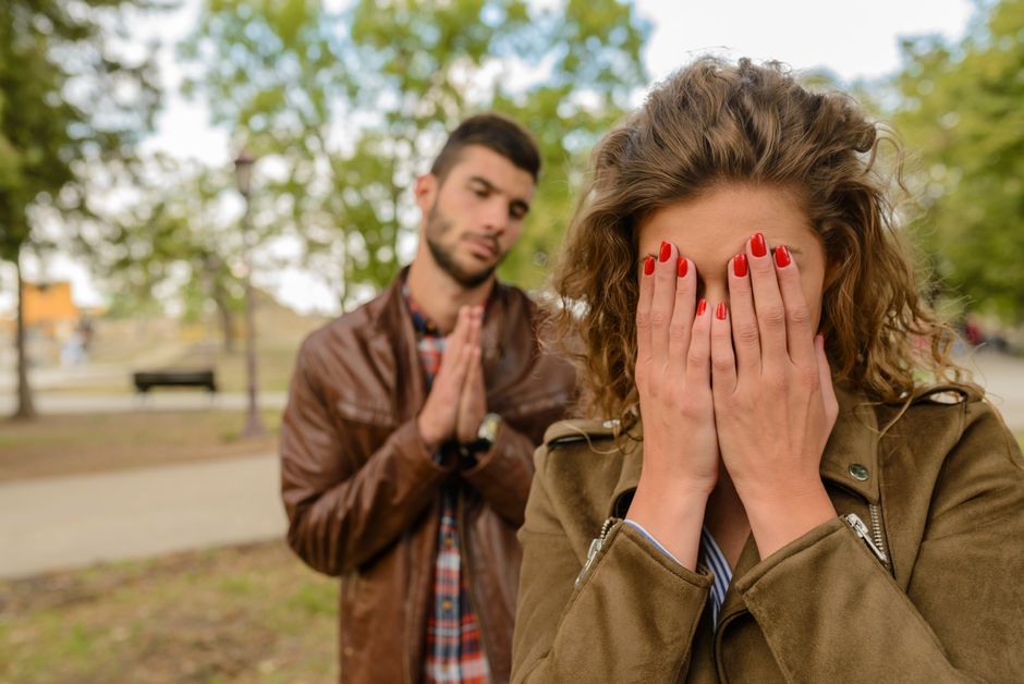 A man silently apologizing with a pleading gesture while a woman covers her face, illustrating the idea of apologizing without over-explaining.