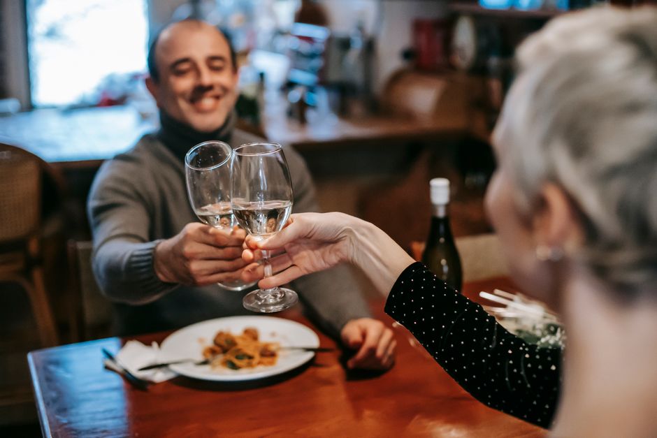 A couple clinking wine glasses at a restaurant dinner, celebrating together.