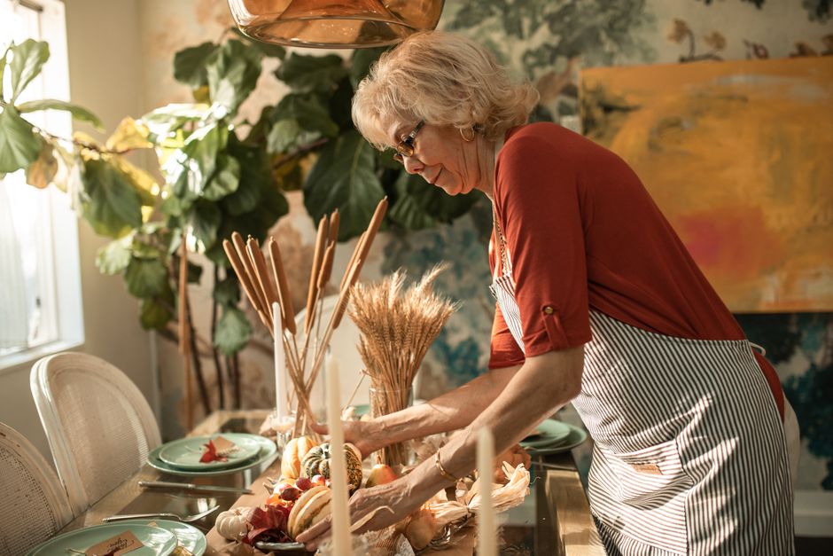 An older woman sets up an elaborate holiday table by herself, illustrating the burden of always hosting.