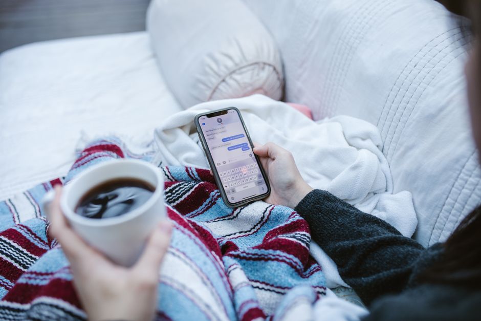 A woman cozily curled up with coffee, calmly checking her phone instead of her group chats.