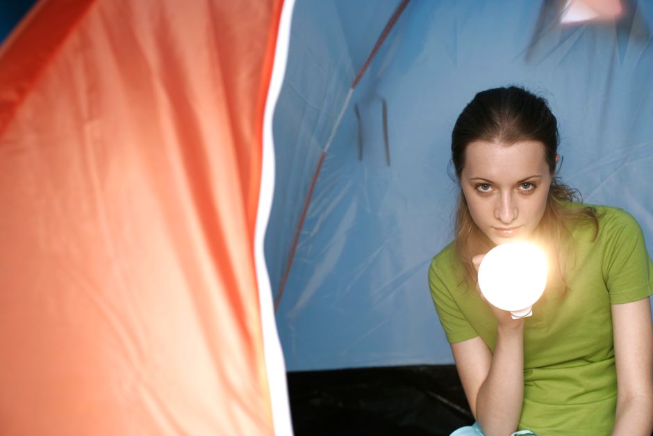A woman looking unimpressed while sitting in a tent at night, reflecting mixed feelings about camping traditions.