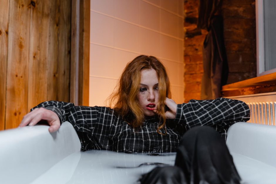 A woman sits fully clothed in a bathtub, looking exhausted rather than relaxed, showing that a bath isn't always the treat it's made out to be.