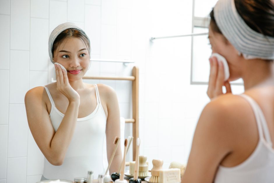 A woman quickly cleanses her face with a cotton pad in front of the bathroom mirror, showing that a skincare routine can be short and still count.