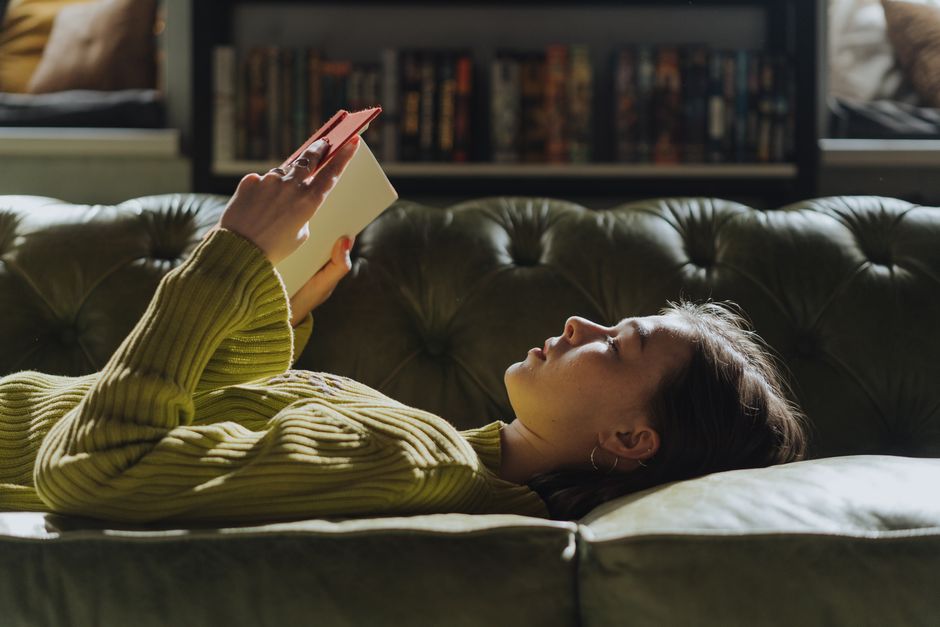 A woman relaxes on a couch simply reading a book, free from any book club pressure.