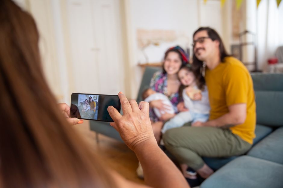A simple, candid family photo being taken on a smartphone, showing a mom, dad, and two kids smiling together on the couch.