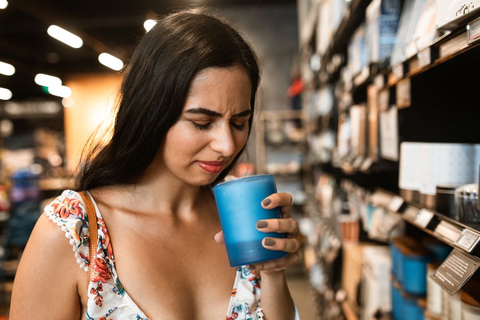 A woman looking unconvinced while smelling a scented candle in a shop, reflecting that not everyone enjoys scented candles.