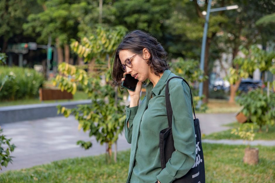 A woman walks alone outside, absorbed in a phone call instead of chatting with others nearby.