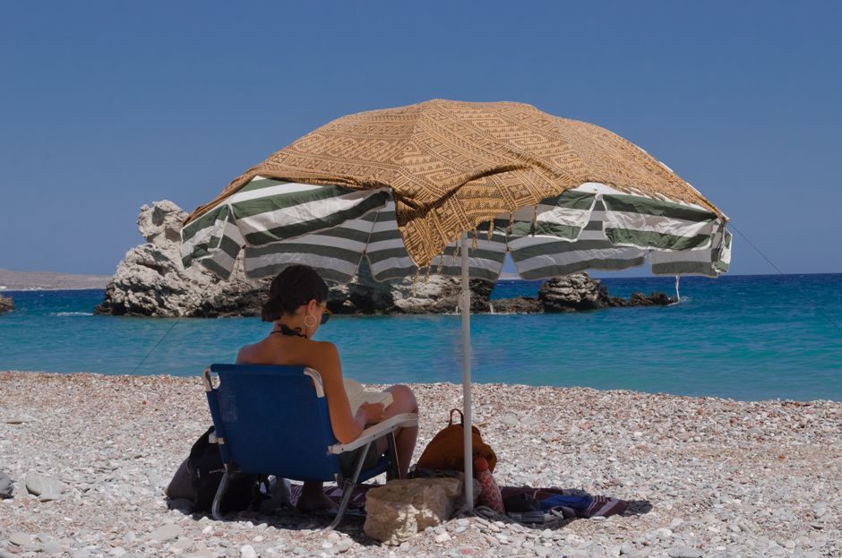 A woman hides from the sun's heat under a big umbrella instead of sunbathing on the hot beach.
